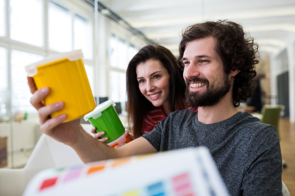 Male and female graphic designers holding plastic container in office